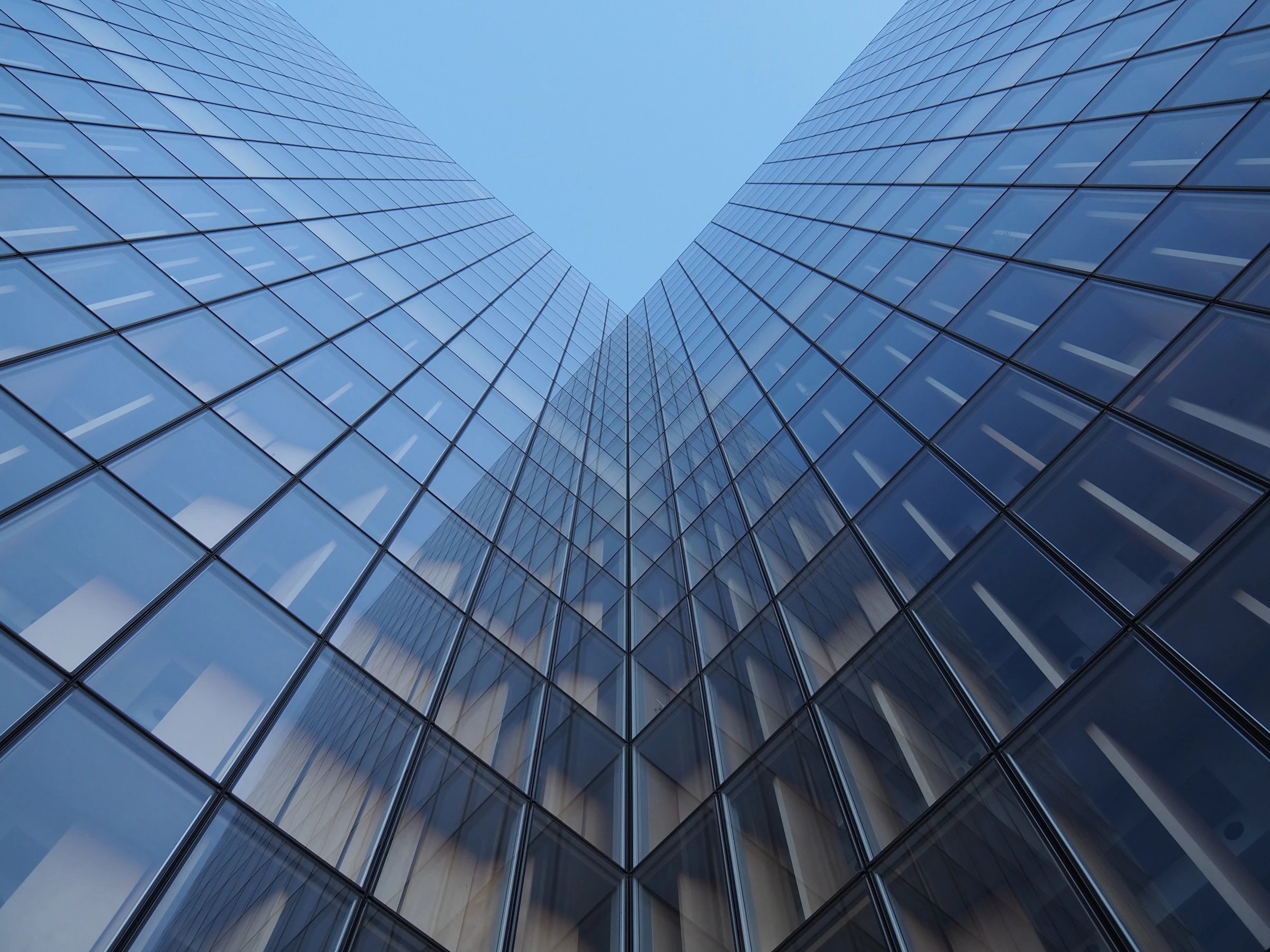 Looking up at the glass walls of two office towers against a blue sky